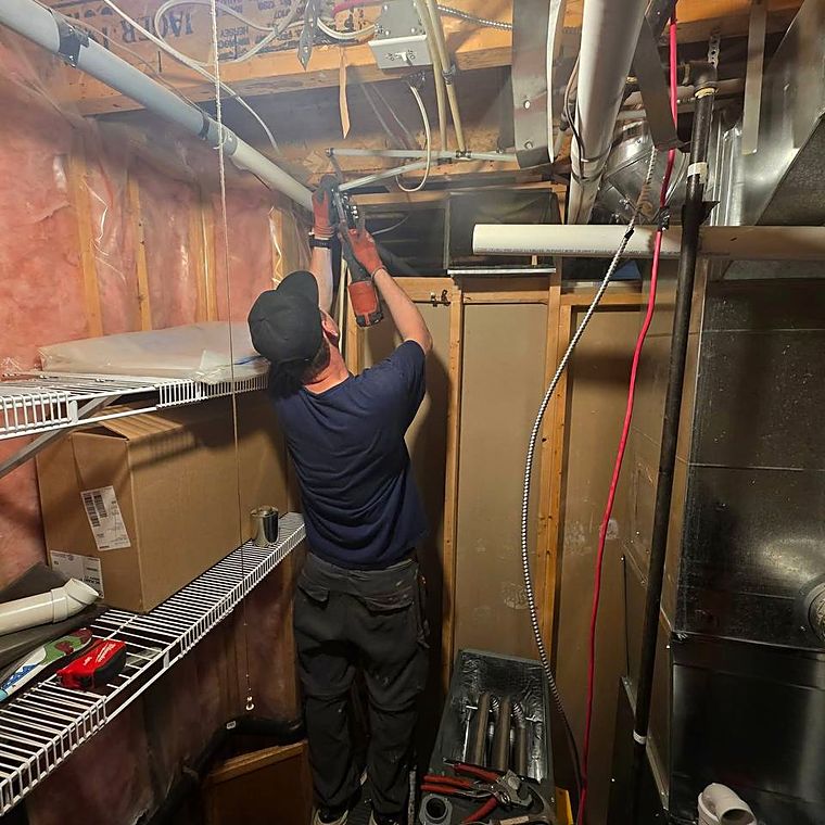 A technician working overhead on ductwork in a basement