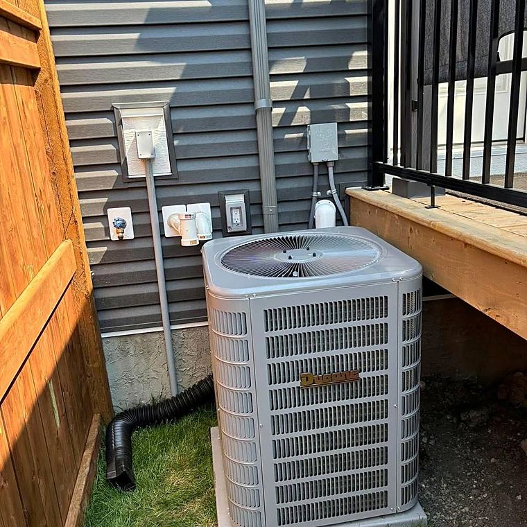 An air conditioner set on a pad beside a fence